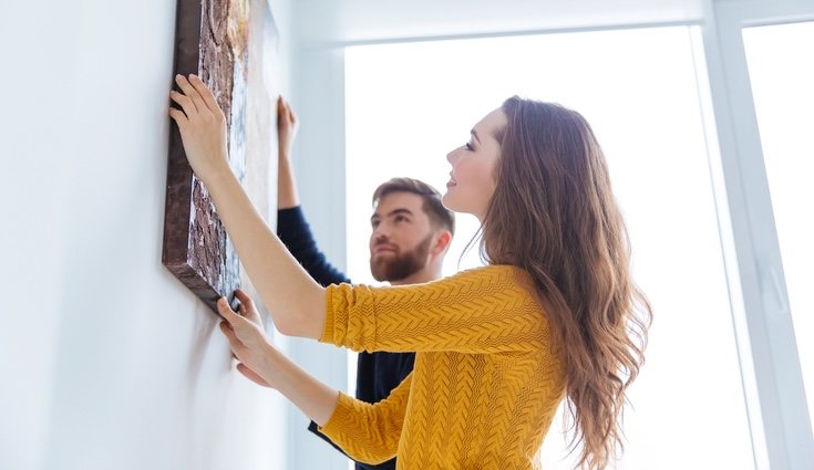 Pareja colgando cuadros en el salón